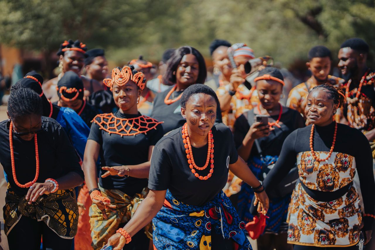 Group of adults in traditional African attire celebrating with a vibrant cultural dance outdoors.